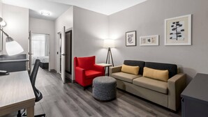 A modern living room with a red armchair, a grey ottoman, a beige sofa, and a desk with a lamp. - Country Inn & Suites by Radisson, Tucson Airport, AZ (Tucson)