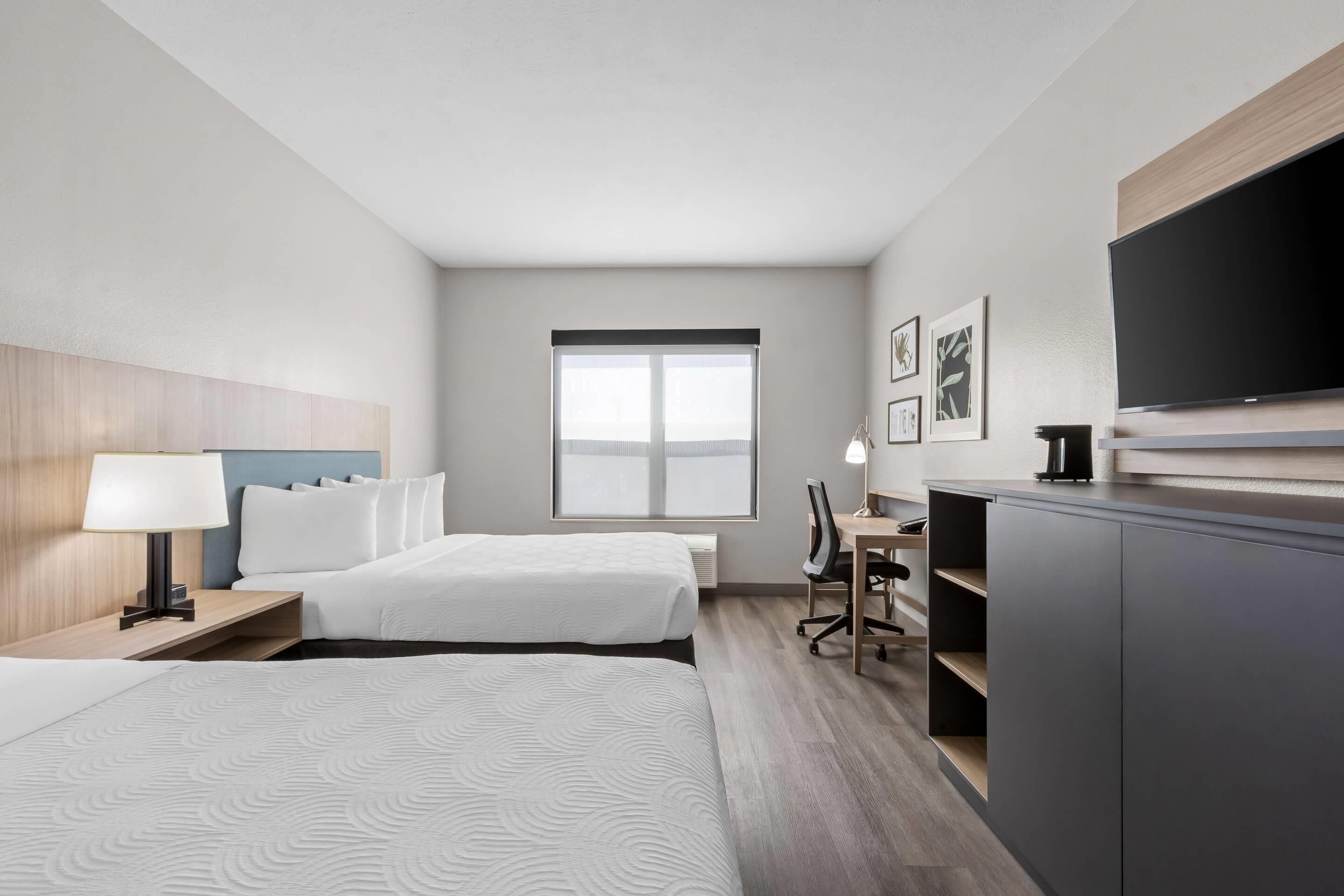 A hotel room with two beds, a desk, a chair, a television, and a window.
