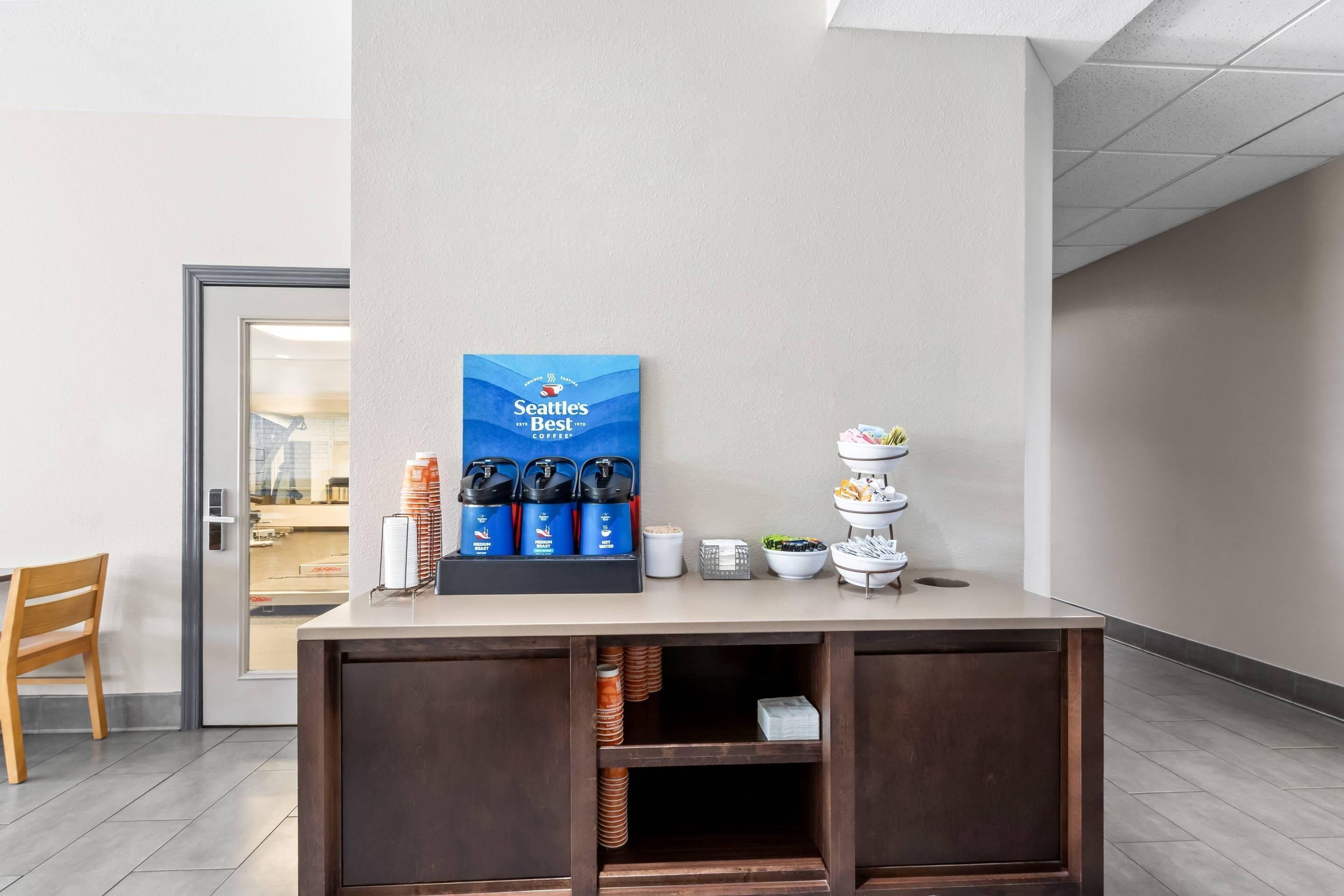A reception desk with a coffee station, a framed sign, and a view into the room.