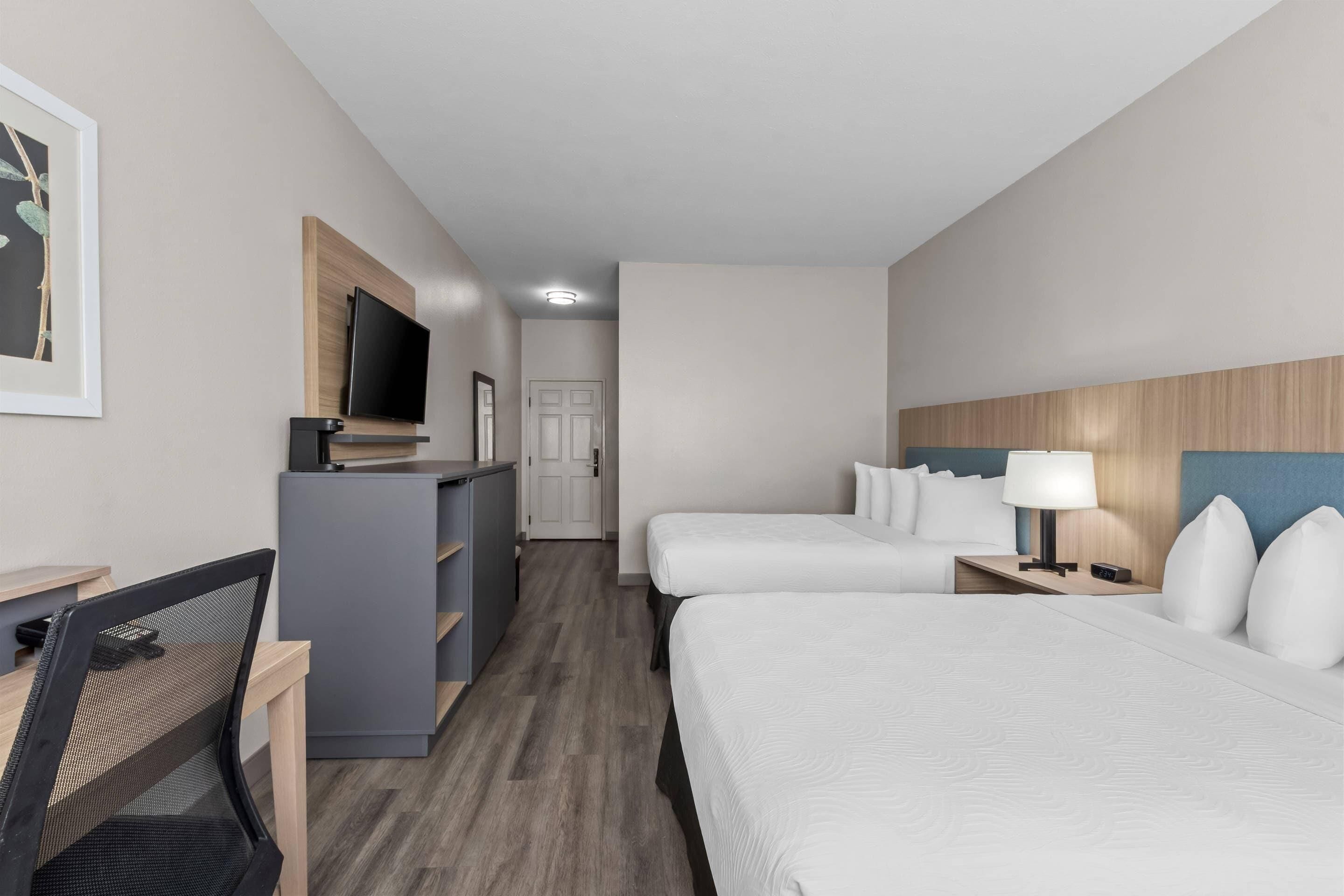 Habitación de hotel con escritorio, dos camas, televisor y puerta.