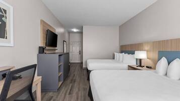 Habitación de hotel con escritorio, dos camas, televisor y puerta.