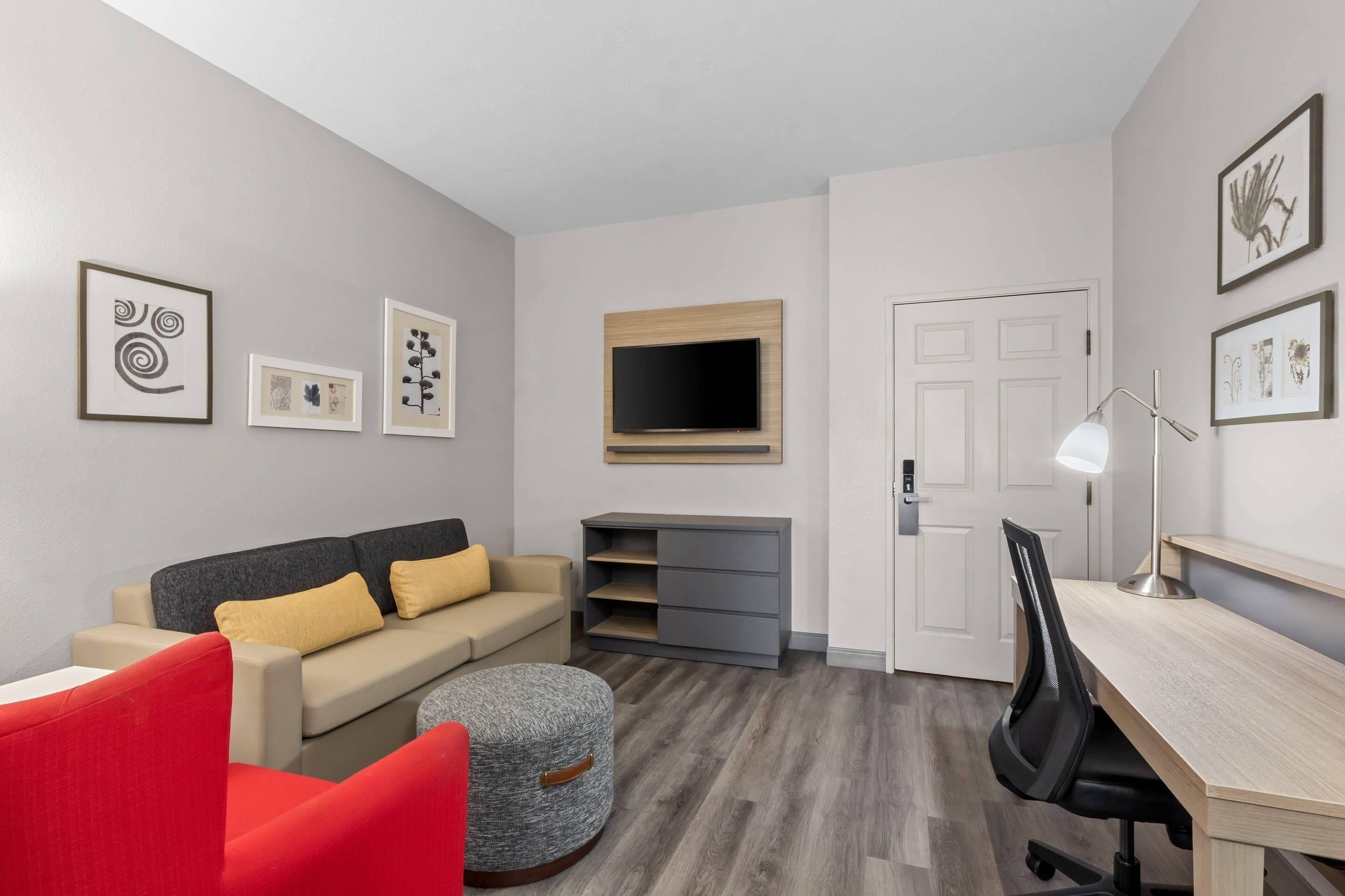 Ein modernes Wohnzimmer mit Sofa, Hocker, Fernseher und einem Schreibtisch mit Stuhl.