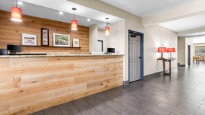 A reception area with a wooden counter, pendant lights, framed pictures, a television, and a door. - Country Inn & Suites by Radisson, Tucson Airport, AZ (Tucson)