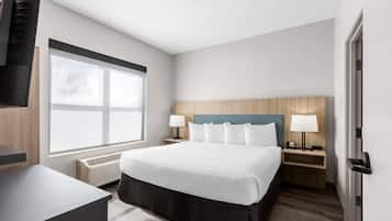 A hotel room with a bed, bedside tables, a desk, a window, and a door.