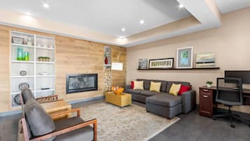 Uma sala de estar moderna com sofá, poltrona, televisão, lareira e objetos decorativos.