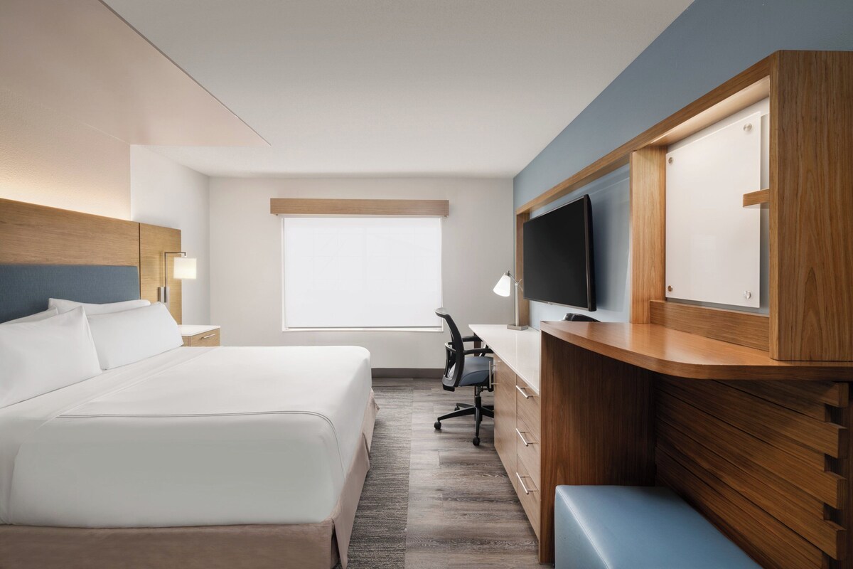 A hotel room with a bed, desk, chair, TV, and wooden cabinets.