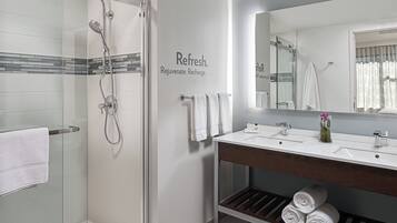 A modern bathroom with a glass shower enclosure, a vanity with a mirror, and a shelf with rolled towels.