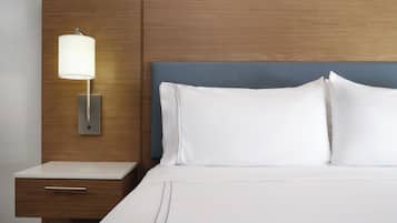 A neatly made bed with white linens and a blue headboard, a bedside table with a lamp, and a wooden panel wall.