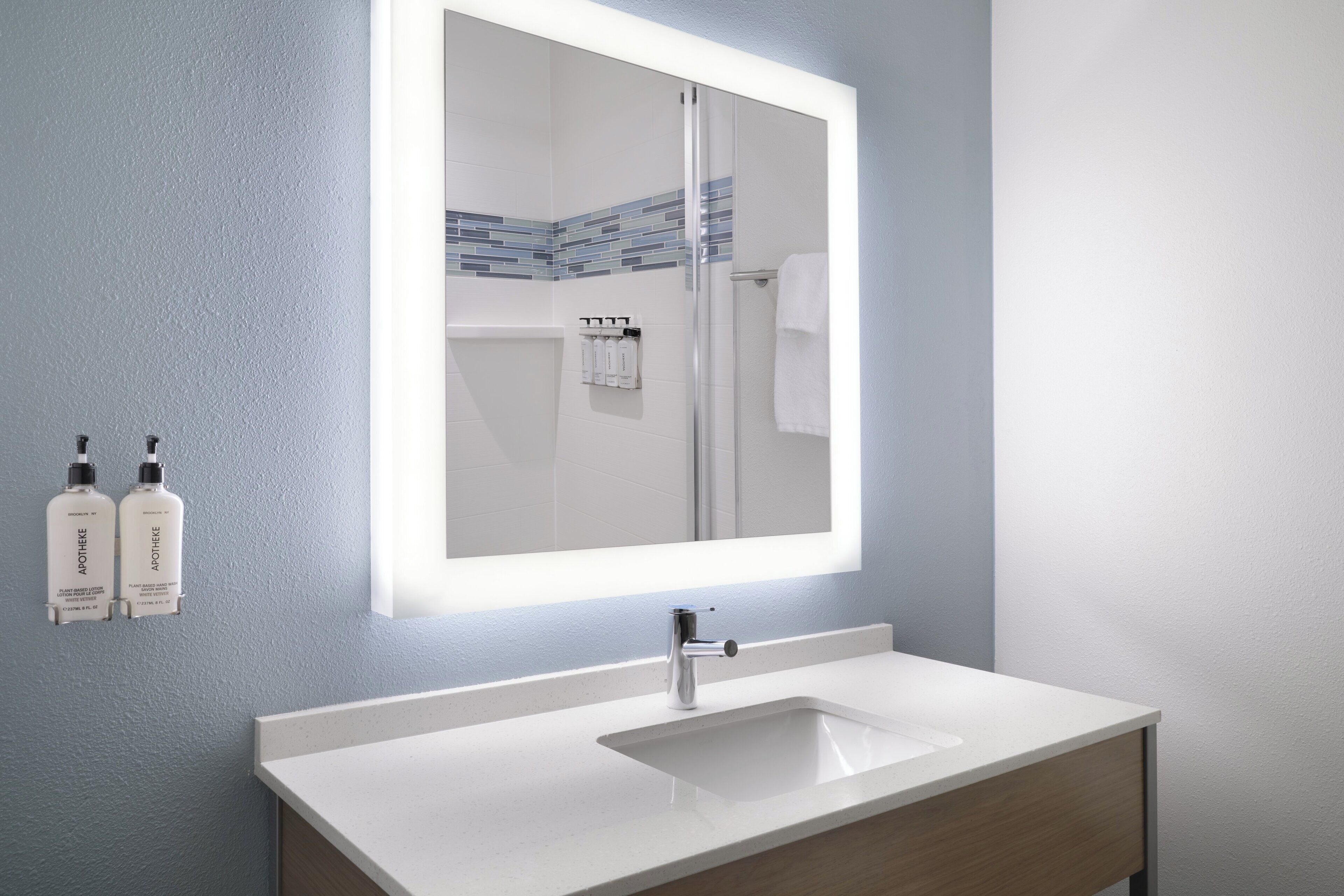 Een badkamer met een wit wastafel, een spiegel en twee flessen toiletartikelen aan de muur.
