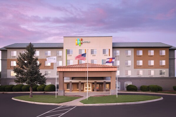 A hotel with a modern facade, multiple flags, and a well-maintained lawn.