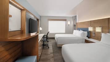 A hotel room with a wooden desk, two beds, a TV, and a window.