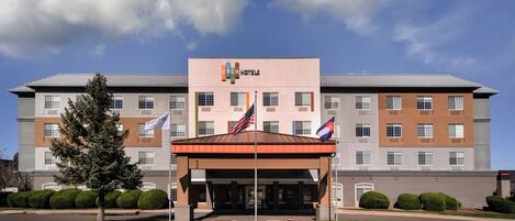 A hotel with a covered entrance, multiple flags, and a well-maintained lawn.