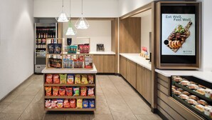 Un présentoir à collations avec divers types de chips et, en arrière-plan, un réfrigérateur pour boissons.