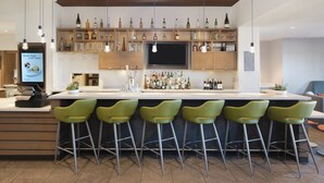 Un espace bar moderne, doté d’un long comptoir, de nombreux tabourets et d’une variété de bouteilles et de verres disposés sur des étagères.