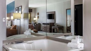 A modern hotel bathroom with a large mirror, a bathtub, a vanity with a sink, and a television.
