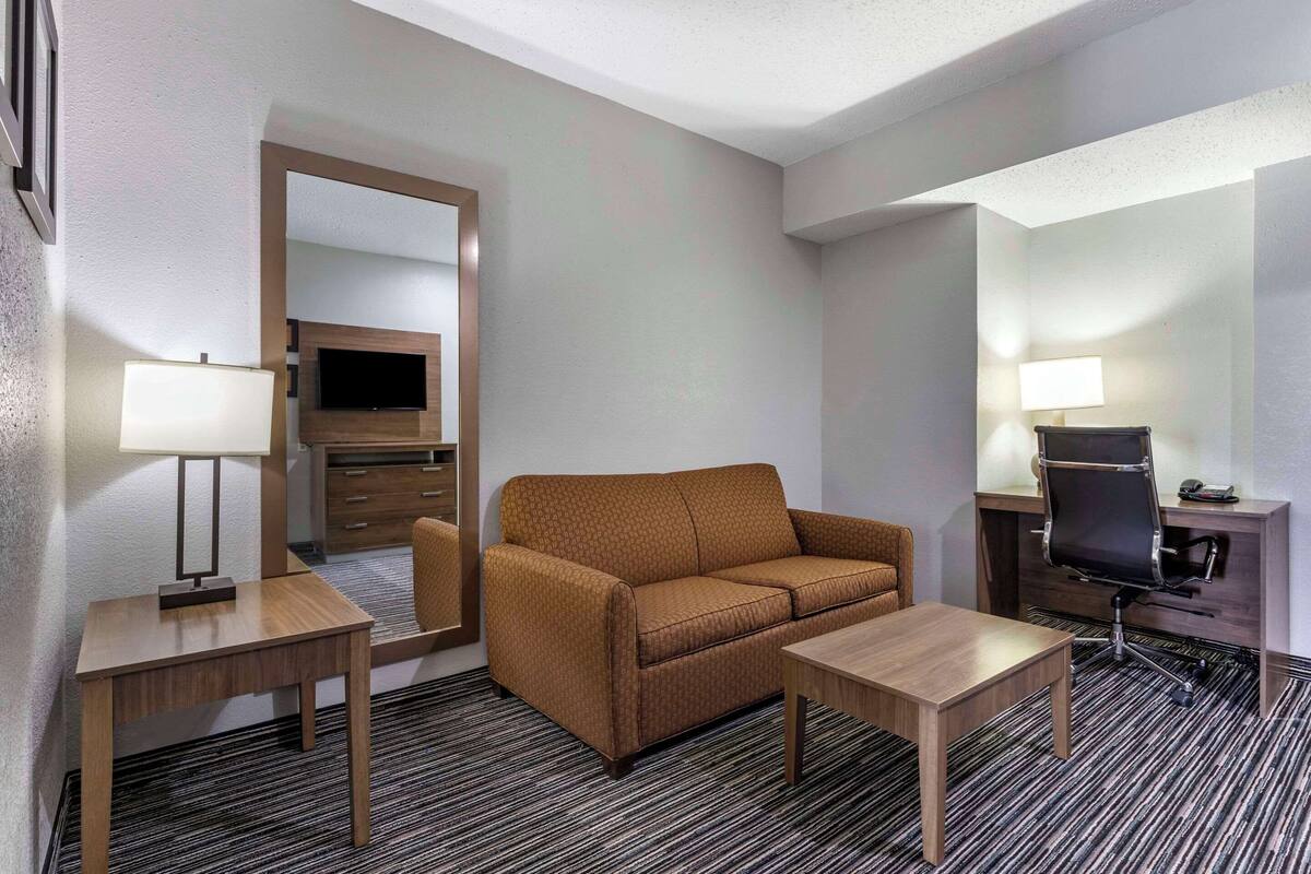 Hotellihuone, jossa on sohva, kaksi pöytää, työpöytä tuolilla, televisio ja peili.
