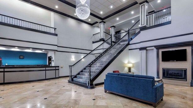 A spacious lobby with a marble floor, a blue sofa, a staircase, a reception desk, and a fireplace.