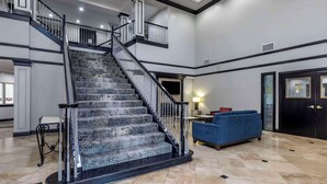 A spacious lobby with a grand staircase, a blue sofa, and a black door.