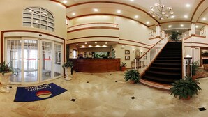 A spacious lobby with a reception desk, a staircase, and a glass door entrance.