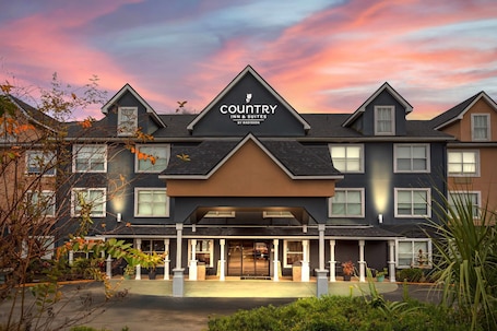 A Country Inn & Suites by Radisson building with a modern architectural design, featuring a prominent entrance and a landscaped front yard.