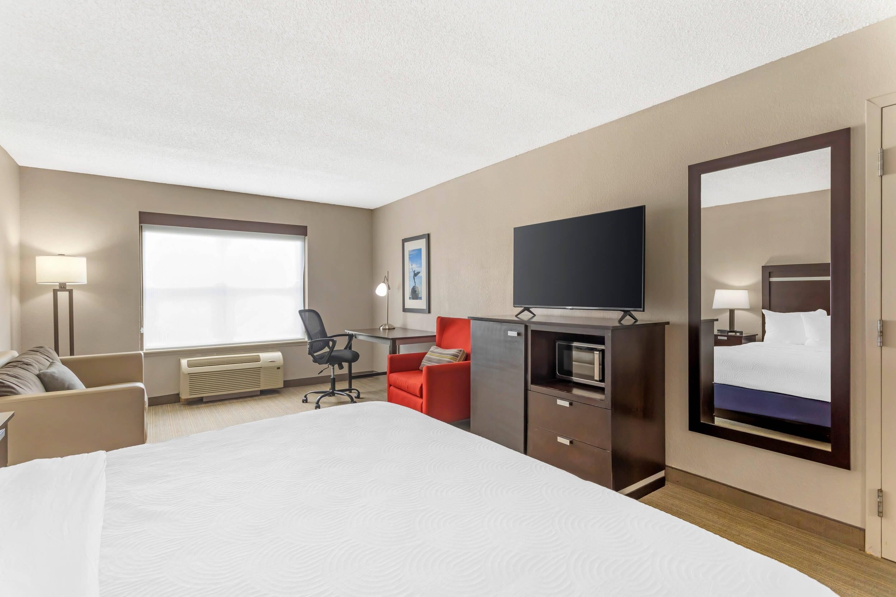 A hotel room with a large bed, a desk, a chair, a TV, a mirror, and a window.