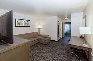 A hotel room with a desk, a sofa, a TV, a lamp, and a patterned carpet.