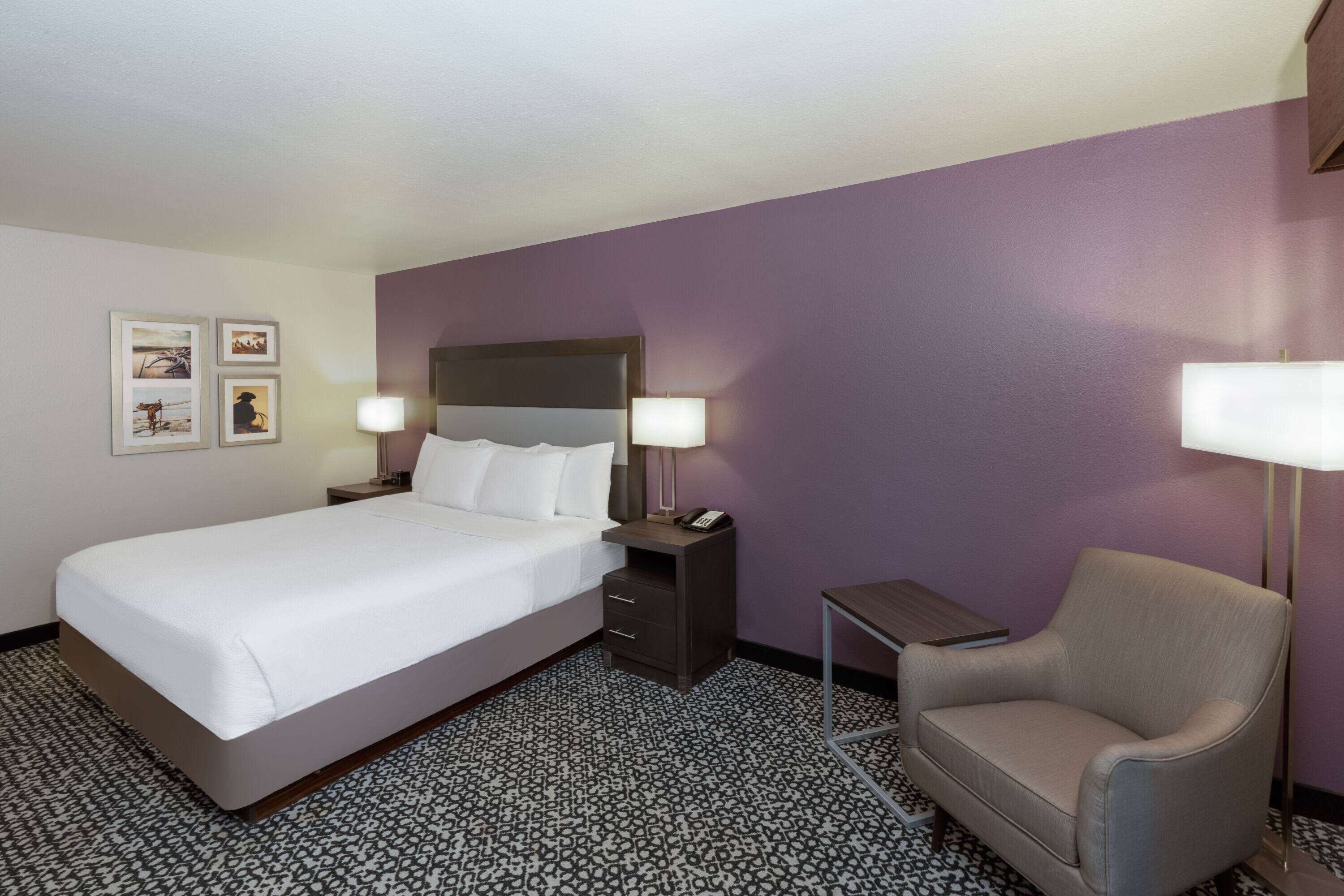 A hotel room with a bed, bedside tables, a chair, and a patterned carpet.