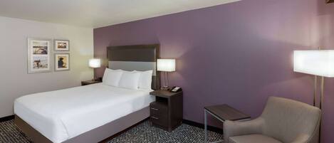A hotel room with a bed, bedside tables, a chair, and a patterned carpet.