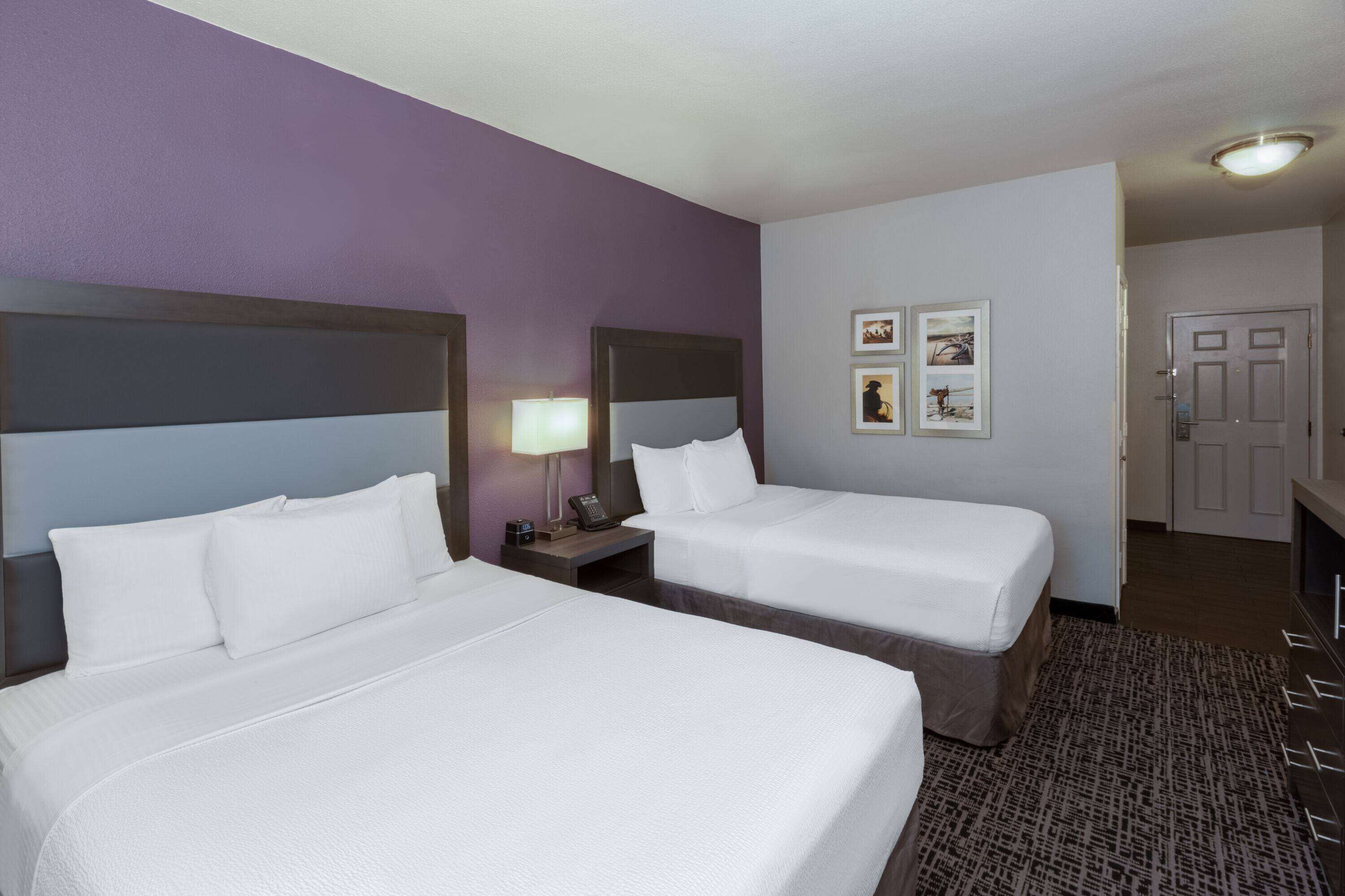 Habitación de hotel con dos camas, una mesita de noche con lámpara y cuadros en la pared.