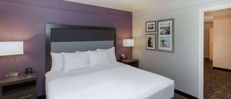 Habitación de hotel con una cama grande, dos mesitas de noche con lámparas, un aparador y cuadros enmarcados en la pared.
