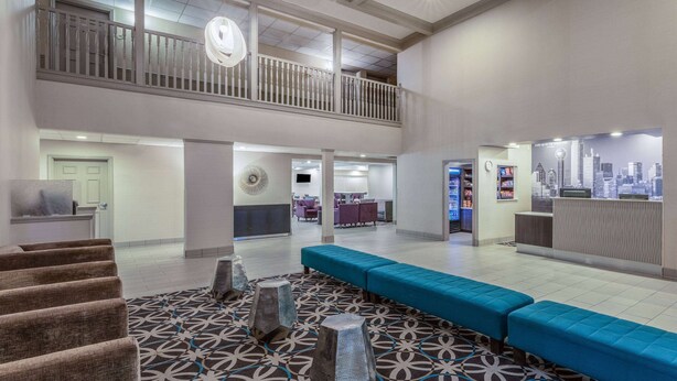 A spacious lobby with a patterned carpet, a blue seating area, and a reception desk with a cityscape backdrop. - La Quinta Inn & Suites by Wyndham Rockwall (Rockwall)