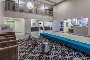 A spacious lobby with a patterned carpet, a blue seating area, and a reception desk with a cityscape backdrop. - La Quinta Inn & Suites by Wyndham Rockwall (Rockwall)