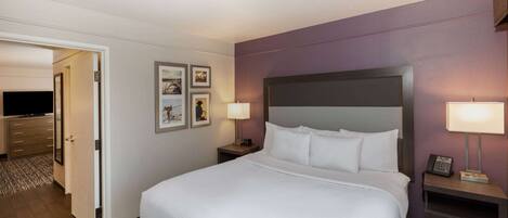 A hotel room with a large bed, a bedside table with a lamp, a TV, and a door leading to a bathroom.