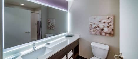 Een moderne badkamer met een grote spiegel, een wit wastafelmeubel, een toilet en een handdoekhouder.