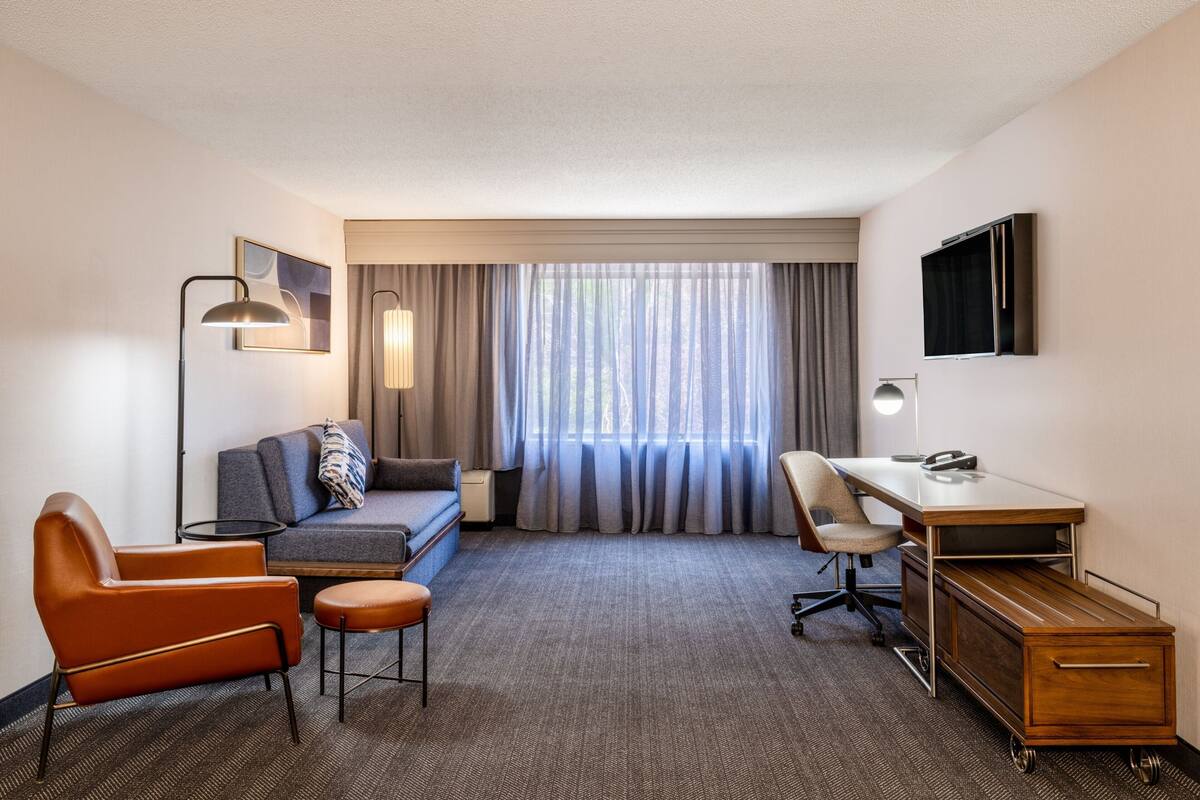 Ein Hotelzimmer mit Sofa, Sessel, Schreibtisch und Fernseher.