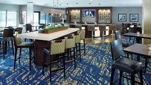 Eine moderne Hotelhalle mit Barbereich, Sitzgelegenheiten und einem gemusterten Teppich.