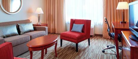 Habitación de hotel con sofá, sillón, mesa de centro, televisor y lámpara.