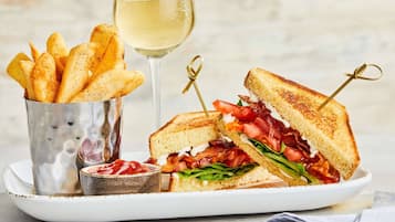 Un plato con un sándwich a la plancha, una copa de vino blanco y un recipiente con papas fritas.