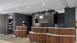 A reception area with a wooden reception desk, a wall-mounted sign, and a shelf with decorative items. - Courtyard by Marriott Providence Downtown (Providence)