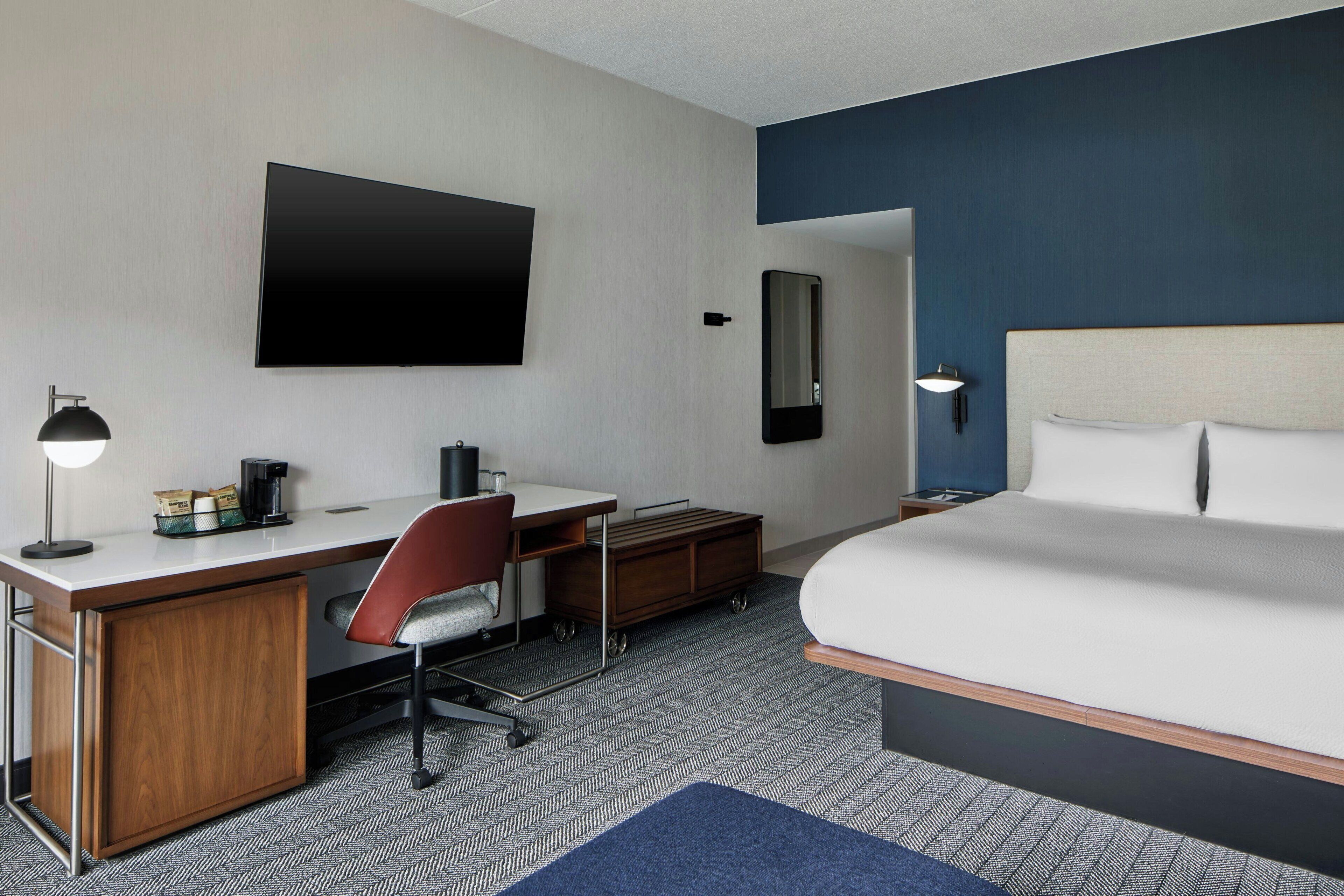Une chambre d’hôtel équipée d’un lit, d’un bureau, d’une chaise, d’une télévision et d’un miroir.