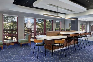 A modern bar area with a wooden counter, bar stools, and large windows offering views of the outdoors. - Courtyard by Marriott Providence Downtown (Providence)