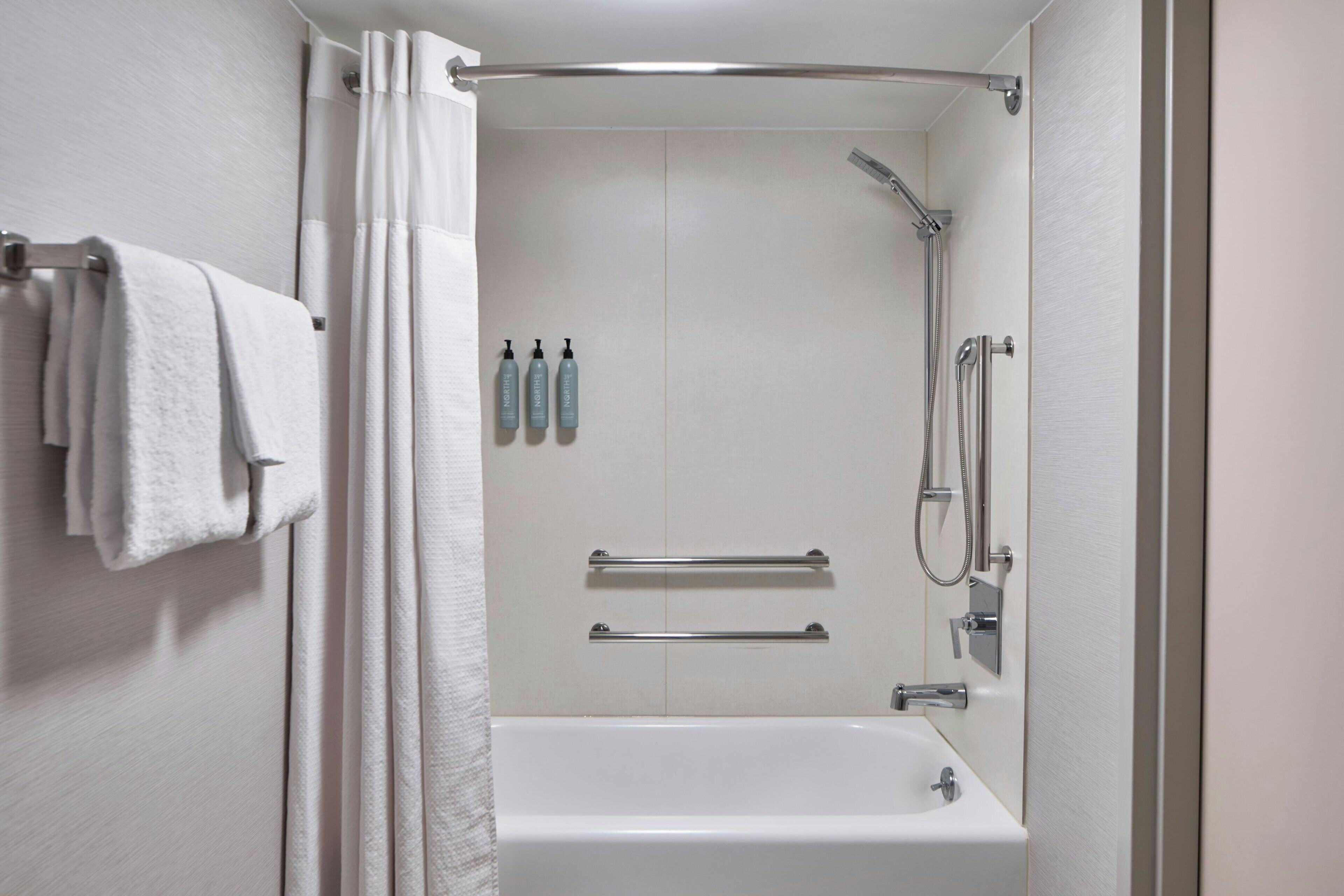 A modern bathroom with a bathtub, shower, and handrails.