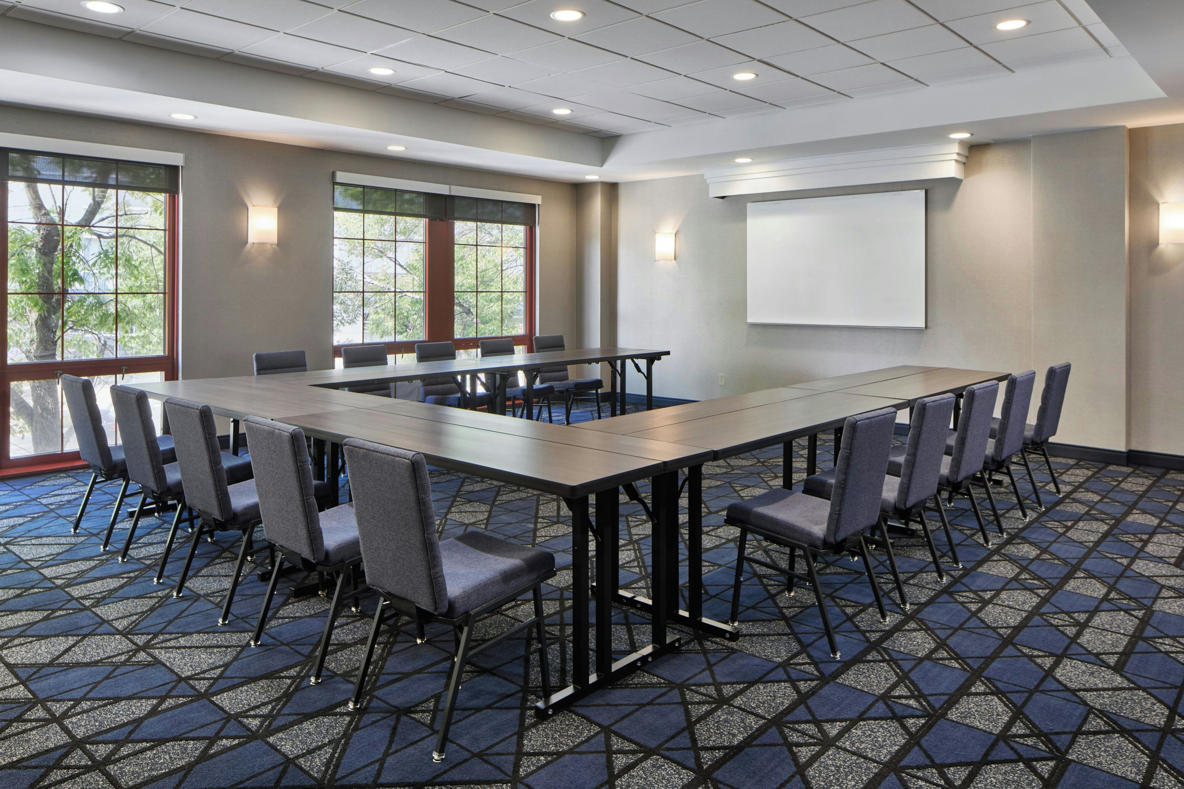 A conference room with a long table, chairs, a projector screen, and large windows.