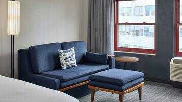 A room with a sofa, a small table, a lamp, a window, and an air conditioning unit.