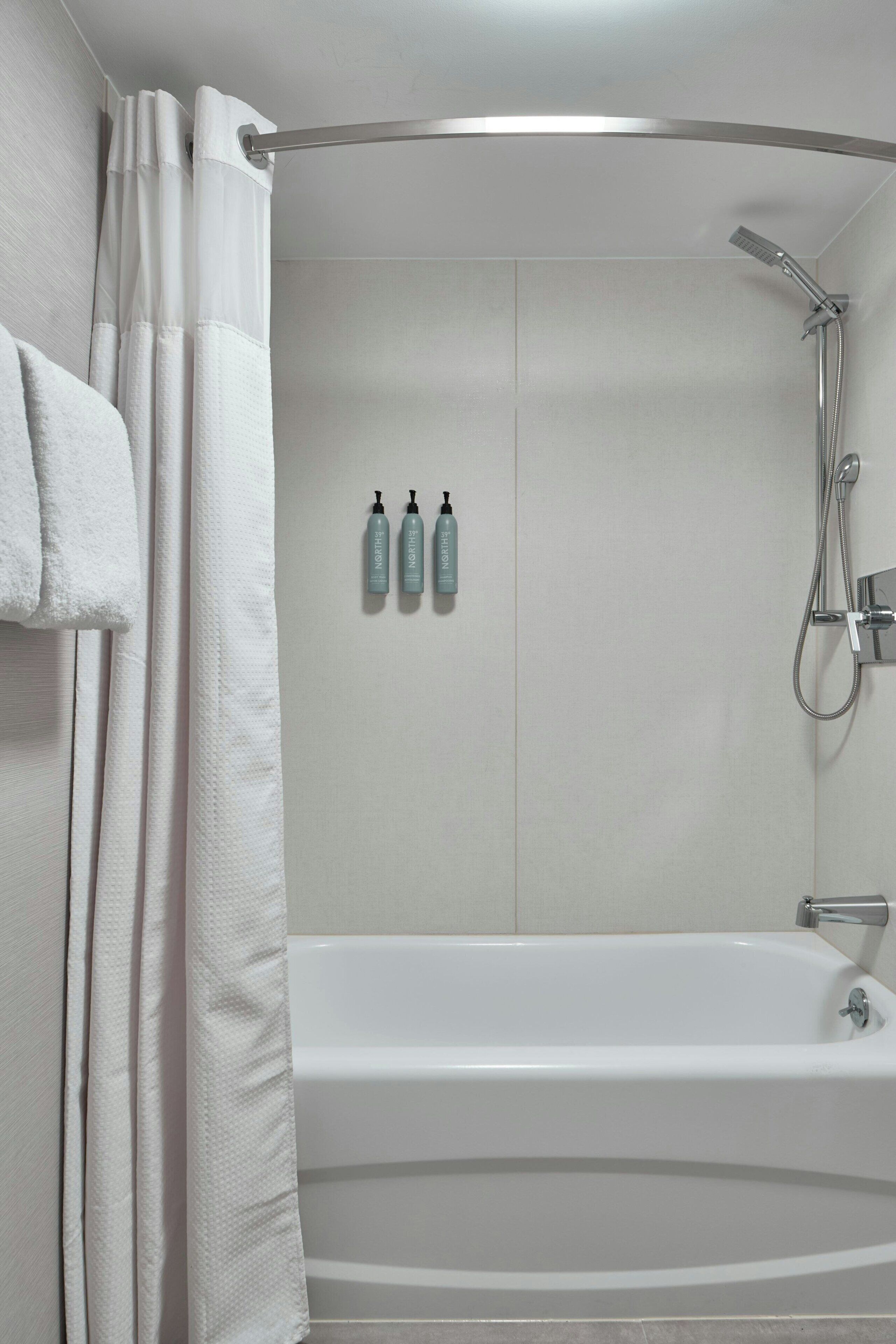 Une salle de bain moderne avec une baignoire, une douche et trois flacons de produits de toilette accrochés au mur.