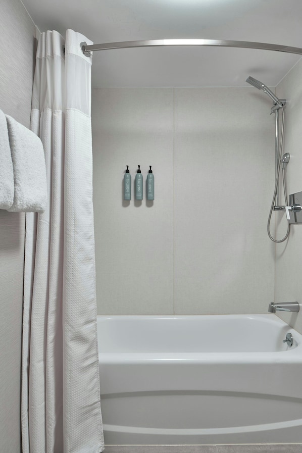 A modern bathroom with a bathtub, shower, and three toiletry bottles on the wall. - Courtyard by Marriott Providence Downtown (Providence)