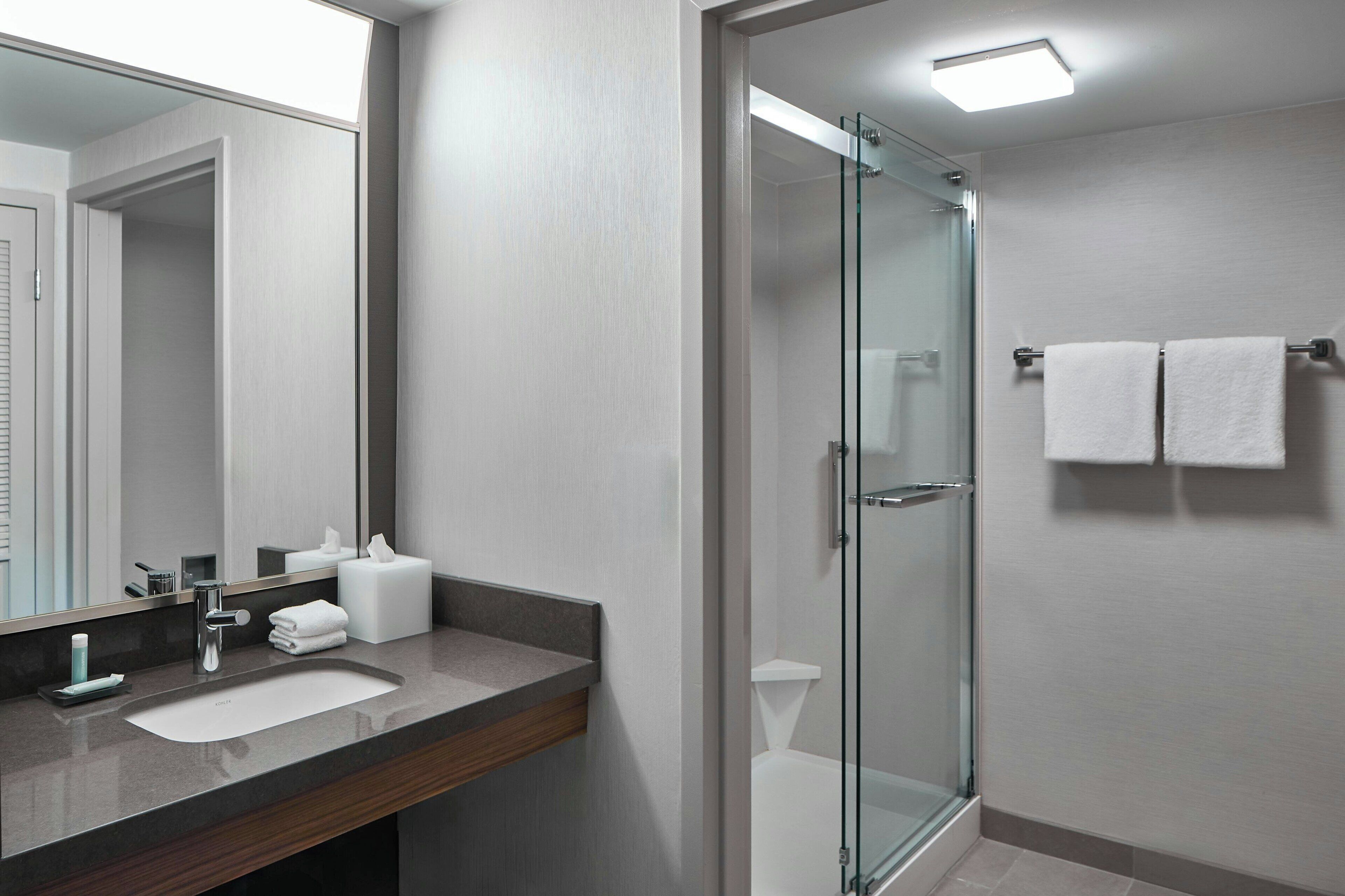 Un baño moderno con cabina de ducha de vidrio, lavabo con espejo y perchero para toallas.