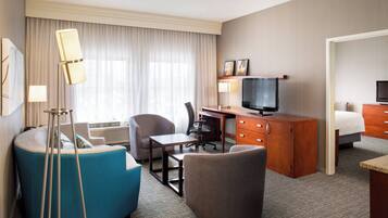 Quarto de hotel com escrivaninha, cadeira, sofá e televisão.