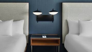 A hotel room with two beds, a nightstand, and wall-mounted lamps.