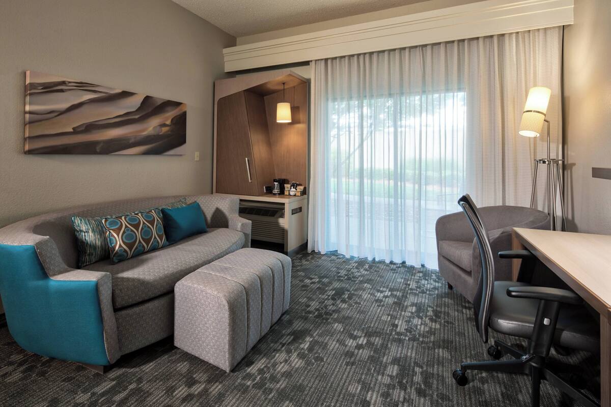 Ein Hotelzimmer mit einer Couch, einem Schreibtisch, einem Stuhl, einer Lampe und einem Bild an der Wand.